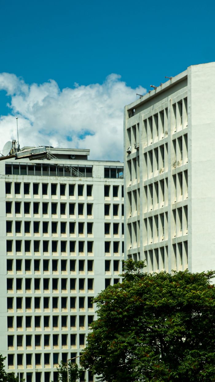 Services Vertical shot of modern high-rise office buildings against a blue sky, featuring dense windows and facade details.